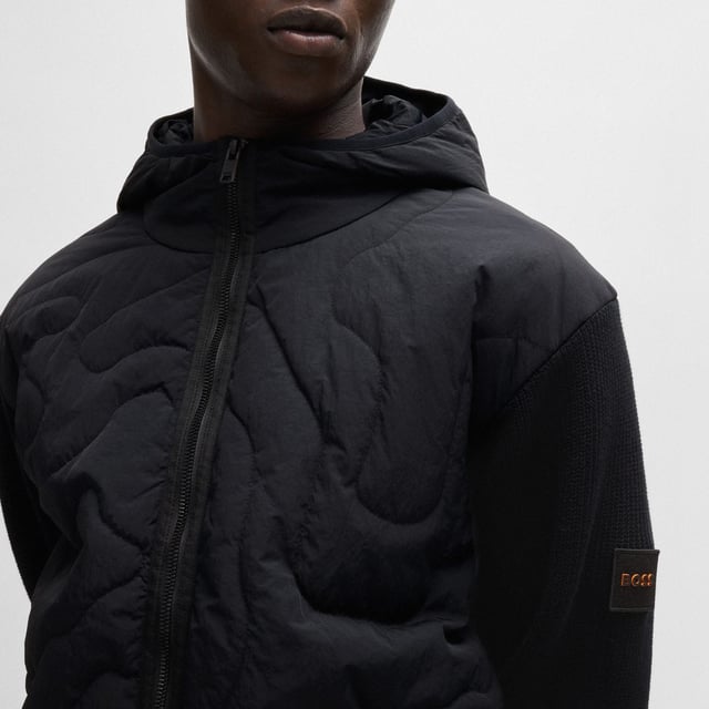 Mens BOSS Kalbero Relaxed Fit Padded Jacket in black.new seasonal design quilting on a light weight padded nylon - sleeves and back in half cardigan rib - double rib hem and cuffs with outside linking - front zip attached on top - visible press button with logo at pockets - squared logo at back inside - light weight padded hood with elasticated binding at opening - new herringbone logo patch at sleeve - 94% cotton 5% polyamide 1% elastane