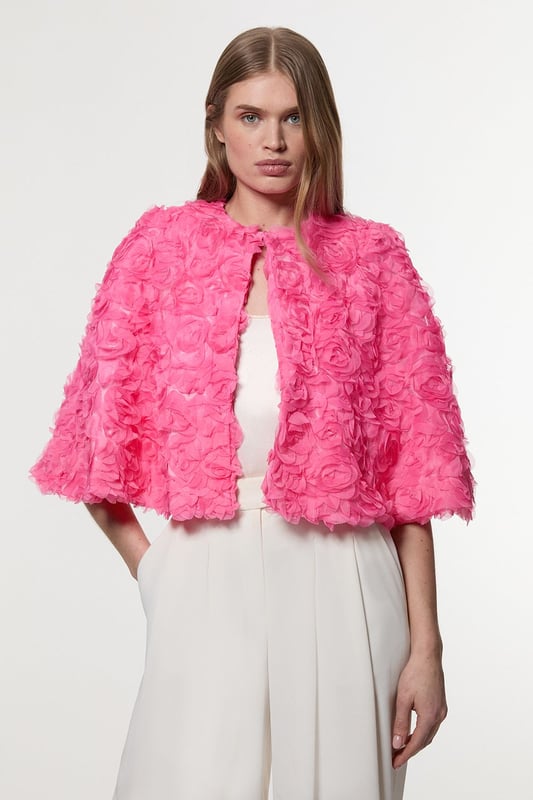 Experience elevated glamour in our cape, which boasts a cropped length, and a textured design with floral appliques. Wear it over a slinky jumpsuit to add an extra level of elegance, or over the matching occasion dress to protect from the elements at upcoming winter events. Textured Rosette Woven Cropped Cape Dramatic Rosette Design Statement Flared Fit Textured, Three Dimensional Floral Applique Cropped Length Matching Dress Sold Separately