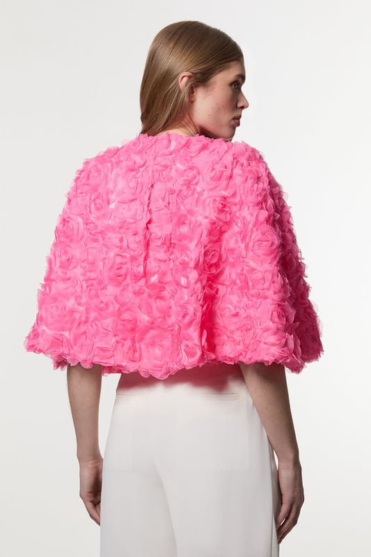 Experience elevated glamour in our cape, which boasts a cropped length, and a textured design with floral appliques. Wear it over a slinky jumpsuit to add an extra level of elegance, or over the matching occasion dress to protect from the elements at upcoming winter events. Textured Rosette Woven Cropped Cape Dramatic Rosette Design Statement Flared Fit Textured, Three Dimensional Floral Applique Cropped Length Matching Dress Sold Separately