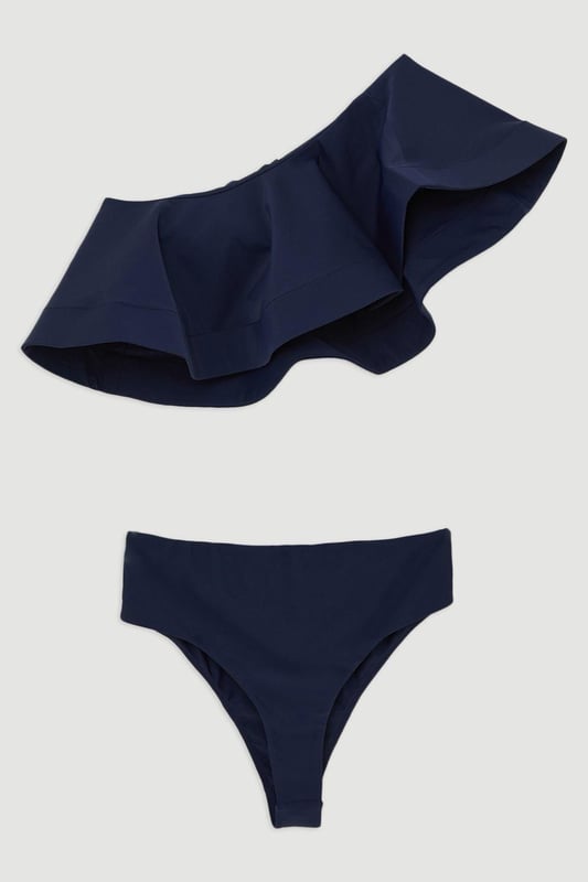 Drama Ruffle One Shoulder Bikini Top Welcome the sun with a bikini that will turn heads, featuring a statement one shoulder design, and a ruffle accent perfect for attracting attention. Style this piece with the matching bikini bottoms, strappy sandals, and a beach cover up for a holiday look that can be reworn time and time again. Drama Ruffle One Shoulder Bikini Top Statement Large Ruffle Detail Flattering One Shoulder Design Comfortable Bandeau Design Matching Bottoms Sold Separately