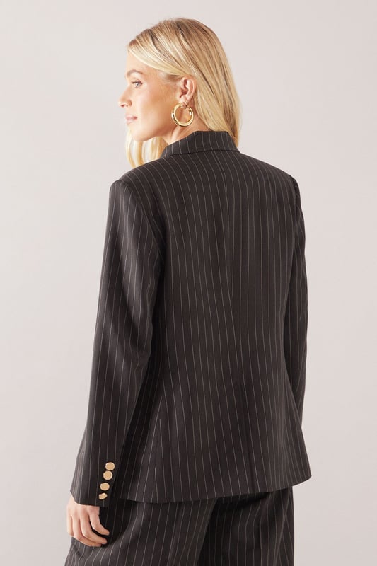 Double-breasted design with striking gold-tone button detailing
        Classic pinstripe pattern for a sophisticated tailored look
        Structured shoulders and notched lapels create a defined silhouette
        Functional front pockets add practicality to this stylish piece
        Comfortable stretch fabric allows for ease of movement throughout the day
    
    This petite double-breasted blazer from Wallis presents the perfect balance of sophistication and contemporary style. The timeless pinstripe pattern creates a refined aesthetic that works beautifully for both office settings and social occasions. Pair with the matching trousers as seen on our model for a coordinated suit look that conveys confidence and poise, or style with dark denim jeans and a simple camisole for a more relaxed approach. The gold-tone buttons add a touch of glamour that's characteristic of the Wallis brand. Perfect for family gatherings when styled with flat shoes and statement jewellery, or dress up with heels and a clutch bag for more formal events. The petite proportions ensure a flattering fit for smaller frames without compromising on style or comfort.