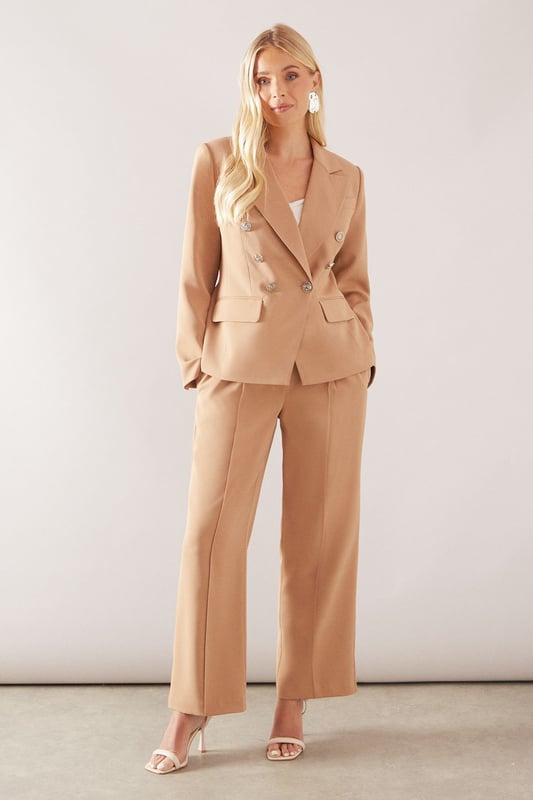 Double-breasted design with striking metallic button detailing for a sophisticated silhouette
        Tailored notched lapels that frame the face beautifully
        Structured shoulders creating a refined, feminine shape
        Functional front flap pockets adding practical elegance
        Decorative sleeve buttons that enhance the tailored finish
    
    This petite double-breasted blazer offers the perfect balance of sophistication and contemporary style. Designed specifically for smaller frames, it creates a flattering silhouette without overwhelming your proportions. The structured shoulders and defined waist work harmoniously to create a polished look suitable for both professional settings and formal occasions. Style with the matching trousers as seen on our model for a coordinated suit ensemble, or pair with slim-fit trousers and heels for a business meeting. For evening events, layer over a silk camisole and add statement jewellery like the drop earrings shown. The versatile design transitions seamlessly from day to night, making it an essential wardrobe investment for the woman who appreciates timeless glamour with modern sensibility.