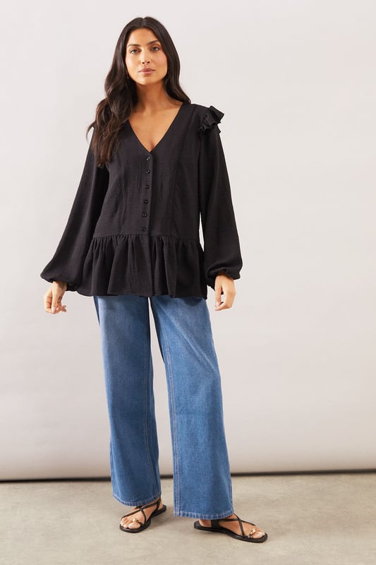 Elegant V-neckline with button-through front detail
        Charming shoulder ruffle trim for a feminine touch
        Relaxed smock silhouette with gathered peplum hem
        Voluminous long sleeves with subtle gathering at cuffs
        Delicate lace trim detailing adds sophisticated texture
    
    This Wallis woven smock top combines comfort with sophisticated style. The flattering V-neckline frames the dcolletage beautifully, whilst the ruffle trim at the shoulders adds a touch of playful femininity. The relaxed fit and peplum hem create a figure-flattering silhouette that drapes gracefully over the body. Style with wide-leg jeans and flat sandals as seen on our model for a chic daytime look perfect for weekend brunches or casual family gatherings. Alternatively, pair with tailored trousers and ballet flats for a smart-casual ensemble ideal for lunch dates or shopping trips. The versatile design transitions effortlessly from day to evening - simply swap your flats for a block heel and add statement earrings for dinner with friends.