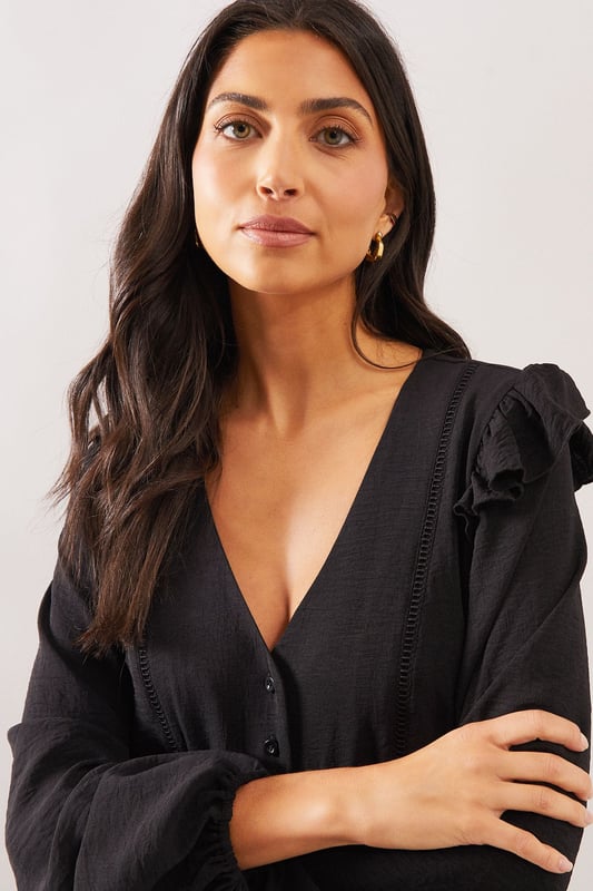 Elegant V-neckline with button-through front detail
        Charming shoulder ruffle trim for a feminine touch
        Relaxed smock silhouette with gathered peplum hem
        Voluminous long sleeves with subtle gathering at cuffs
        Delicate lace trim detailing adds sophisticated texture
    
    This Wallis woven smock top combines comfort with sophisticated style. The flattering V-neckline frames the dcolletage beautifully, whilst the ruffle trim at the shoulders adds a touch of playful femininity. The relaxed fit and peplum hem create a figure-flattering silhouette that drapes gracefully over the body. Style with wide-leg jeans and flat sandals as seen on our model for a chic daytime look perfect for weekend brunches or casual family gatherings. Alternatively, pair with tailored trousers and ballet flats for a smart-casual ensemble ideal for lunch dates or shopping trips. The versatile design transitions effortlessly from day to evening - simply swap your flats for a block heel and add statement earrings for dinner with friends.