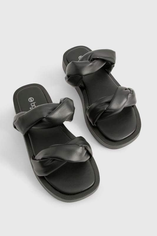 Wide fit design for enhanced comfort and easy wear
        Distinctive twisted strap detail adding contemporary flair
        Flat sole with height between 0-2cm for all-day wearability
        Smooth PU construction offering a sleek, polished finish
        Cushioned footbed providing essential support for extended wear
    
    These statement slides redefine casual footwear with their eye-catching twisted strap detail. The wide fit design ensures maximum comfort whilst the flat sole makes them perfect for those busy days when style can't compromise practicality. Pair with cropped wide-leg trousers and an oversized linen shirt for a sophisticated daytime look, or team with a flowing maxi dress for relaxed weekend brunches. The versatile design transitions effortlessly from poolside lounging to casual city strolls. Their minimalist aesthetic works brilliantly with both neutral tones and vibrant outfits, making them a wardrobe essential for the fashion-forward woman who values both comfort and contemporary style. Ideal for family gatherings, festival outings, or holiday explorations when you need footwear that's as reliable as it is stylish.