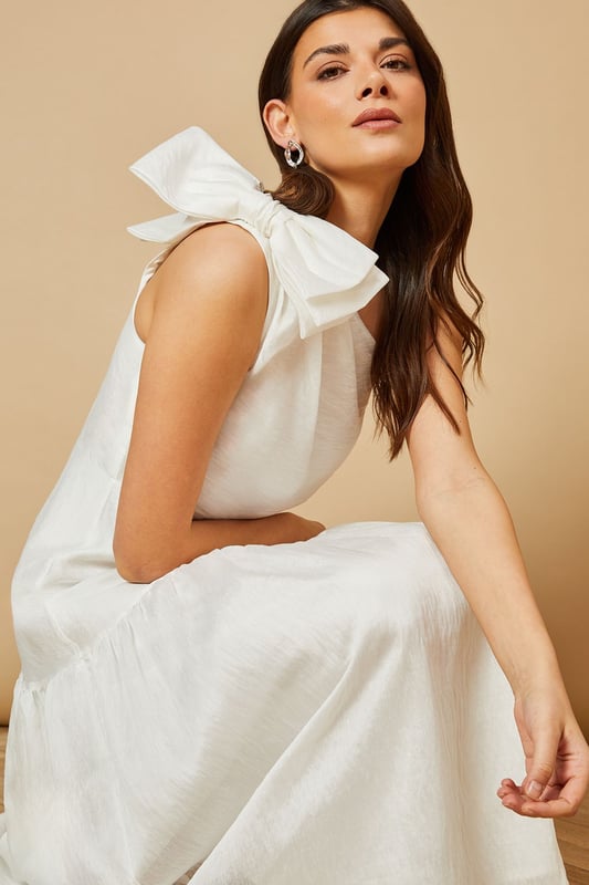 Striking one-shoulder design with an elegant oversized bow detail
        Feminine midi length with a flattering tiered skirt
        Lightweight Tencel fabric that drapes beautifully
        Clean, minimalist silhouette perfect for special occasions
        Versatile design that can be dressed up or down with accessories
    
    This enchanting one-shoulder midi dress showcases Oasis's signature feminine aesthetic with its standout bow shoulder detail. The graceful tiered skirt creates movement and dimension whilst maintaining a sophisticated silhouette. Style with strappy heeled sandals and statement earrings for summer weddings or garden parties. For race day events, pair with a fascinator and clutch bag for a refined ensemble. The versatile design transitions beautifully from daytime celebrations to evening soires-simply switch your accessories to match the occasion. The clean lines and classic shape make this dress a timeless addition to your occasion wardrobe, whilst the midi length offers both elegance and practicality. Perfect for those moments when you want to make a subtle yet memorable impression.