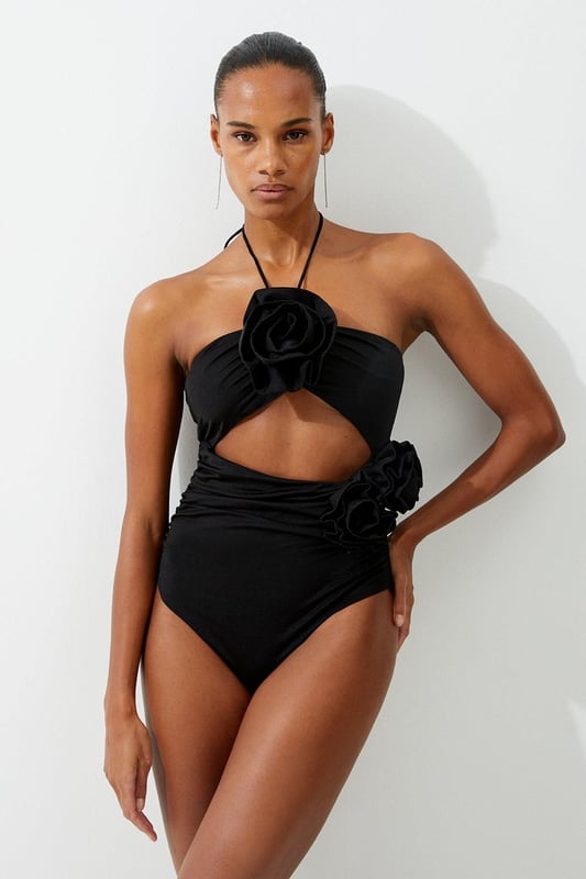 Welcome the sun with a swimming costume that will turn heads, featuring a three dimensional corsage accent on the bust and hip, and a statement cut out design in the front and back. Style this piece with strappy sandals and a beach cover up for a holiday look that can be reworn time and time again. Rosette Cut Out Detail Swimsuit Flattering Halter Neckline Unique, Three Dimensional Flower Accent Statement Cut Out Design Tie and Clasp Fastening in Back