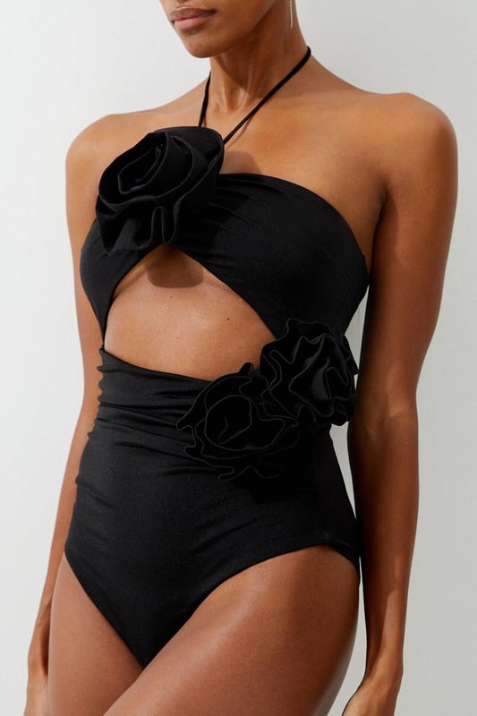 Welcome the sun with a swimming costume that will turn heads, featuring a three dimensional corsage accent on the bust and hip, and a statement cut out design in the front and back. Style this piece with strappy sandals and a beach cover up for a holiday look that can be reworn time and time again. Rosette Cut Out Detail Swimsuit Flattering Halter Neckline Unique, Three Dimensional Flower Accent Statement Cut Out Design Tie and Clasp Fastening in Back