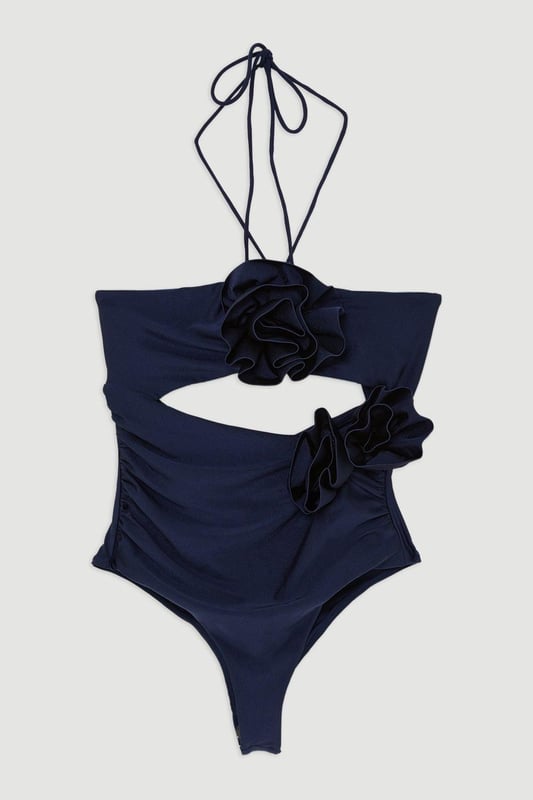 Rosette Cut Out Detail Swimsuit Welcome the sun with a swimming costume that will turn heads, featuring a three dimensional corsage accent on the bust and hip, and a statement cut out design in the front and back. Style this piece with strappy sandals and a beach cover up for a holiday look that can be reworn time and time again. Rosette Cut Out Detail Swimsuit Flattering Halter Neckline Unique, Three Dimensional Flower Accent Statement Cut Out Design Tie and Clasp Fastening in Back