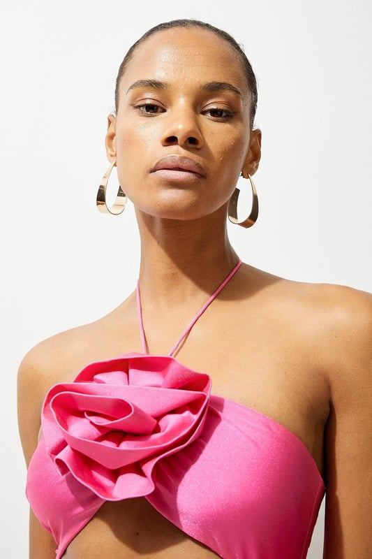 Welcome the sun with a swimming costume that will turn heads, featuring a three dimensional corsage accent on the bust and hip, and a statement cut out design in the front and back. Style this piece with strappy sandals and a beach cover up for a holiday look that can be reworn time and time again. Rosette Cut Out Detail Swimsuit Flattering Halter Neckline Unique, Three Dimensional Flower Accent Statement Cut Out Design Tie and Clasp Fastening in Back
