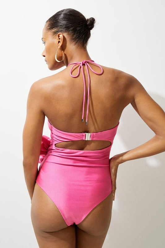 Welcome the sun with a swimming costume that will turn heads, featuring a three dimensional corsage accent on the bust and hip, and a statement cut out design in the front and back. Style this piece with strappy sandals and a beach cover up for a holiday look that can be reworn time and time again. Rosette Cut Out Detail Swimsuit Flattering Halter Neckline Unique, Three Dimensional Flower Accent Statement Cut Out Design Tie and Clasp Fastening in Back