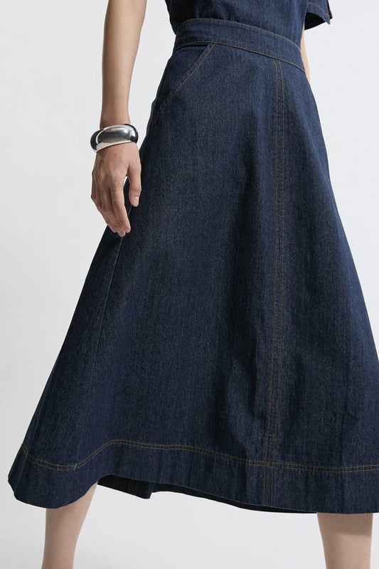 This Karen Millen denim midi skirt is a versatile wardrobe staple that effortlessly bridges the gap between casual and smart-casual attire. The full, flared silhouette creates a graceful movement as you walk, while the high-waisted design accentuates your natural curves. Style it with a fitted knit top and ankle boots for a stylish daytime look, perfect for weekend brunches or casual family gatherings. For a more relaxed vibe, pair it with a simple t-shirt and trainers. The side pockets add a practical touch, ideal for keeping small essentials close at hand. This skirt's adaptable nature makes it suitable for various occasions, from laid-back office days to informal evening outings. Its timeless design ensures it will remain a go-to piece in your wardrobe for seasons to come.  Midi-length denim skirt with a full, flared silhouette High-waisted design for a flattering fit Side pockets for practicality and style Versatile cotton fabric suitable for various seasons Subtle A-line shape creates a feminine profile