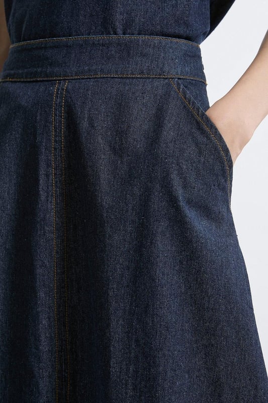 This Karen Millen denim midi skirt is a versatile wardrobe staple that effortlessly bridges the gap between casual and smart-casual attire. The full, flared silhouette creates a graceful movement as you walk, while the high-waisted design accentuates your natural curves. Style it with a fitted knit top and ankle boots for a stylish daytime look, perfect for weekend brunches or casual family gatherings. For a more relaxed vibe, pair it with a simple t-shirt and trainers. The side pockets add a practical touch, ideal for keeping small essentials close at hand. This skirt's adaptable nature makes it suitable for various occasions, from laid-back office days to informal evening outings. Its timeless design ensures it will remain a go-to piece in your wardrobe for seasons to come.  Midi-length denim skirt with a full, flared silhouette High-waisted design for a flattering fit Side pockets for practicality and style Versatile cotton fabric suitable for various seasons Subtle A-line shape creates a feminine profile