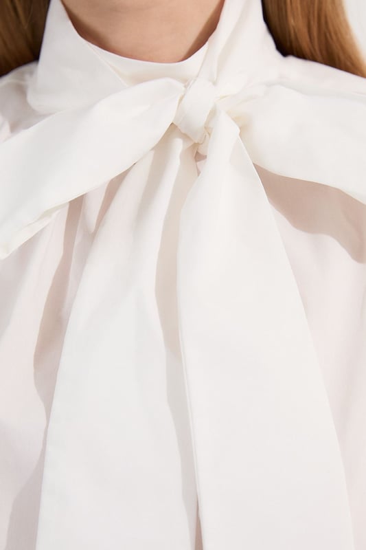 This Karen Millen blouse artfully balances classic femininity with contemporary design elements. The statement pussy bow and dramatic puff sleeves create a silhouette that commands attention whilst maintaining effortless sophistication. Style with high-waisted denim for casual weekend brunches, as seen on our model, or pair with tailored trousers for polished daywear options. The structured cotton poplin fabric holds its shape beautifully throughout the day, making this piece ideal for family gatherings or important daytime meetings. The unexpected back cut-out detail adds interest when viewed from all angles, ensuring you make an impression coming and going. This versatile blouse transitions seamlessly from day to evening; simply swap your trainers for a block heel and add statement jewellery for dinner dates or gallery openings.  Elegant pussy bow detail creates a sophisticated focal point Voluminous puff sleeves add a contemporary silhouette High neckline offers refined coverage for versatile styling Crisp cotton poplin fabric provides structure with breathable comfort Distinctive cut-out back detail introduces an unexpected modern twist