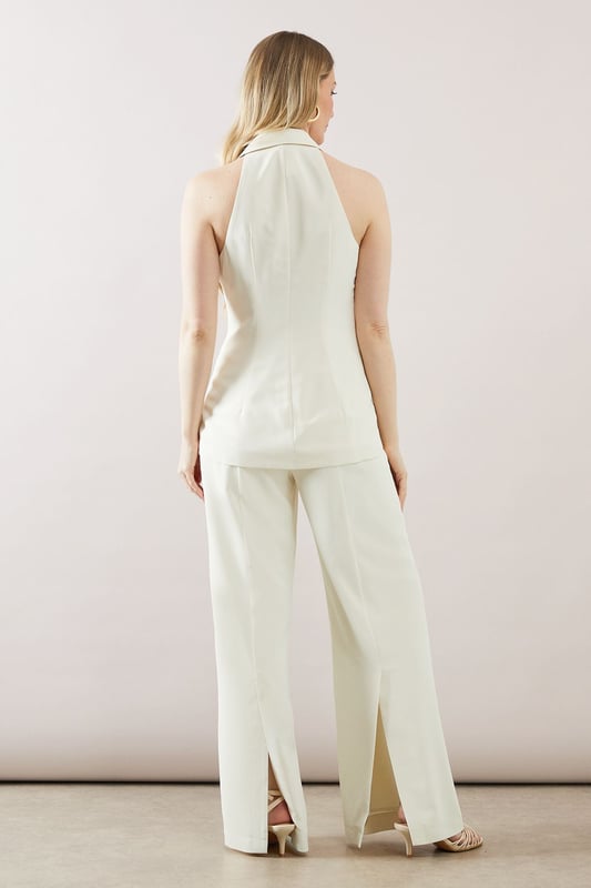Sleek longline waistcoat with a sophisticated collar
        Halterneck design for a modern, chic look
        Wide-leg trousers with a flattering high waist
        Side pockets for practicality and style
        Back split detail on trousers for ease of movement
    
    This collared longline waistcoat ensemble from Wallis is the epitome of contemporary sophistication. Perfect for the woman who appreciates glamour with a comfortable edge, this set is versatile enough for various occasions. The sleek waistcoat, featuring a halterneck design, pairs beautifully with the wide-leg trousers, creating a flowing silhouette that's both flattering and on-trend. For a casual yet polished look, style with minimalist jewellery and strappy sandals. When attending family gatherings or informal events, layer with a lightweight blouse underneath for added dimension. The ensemble's clean lines and elegant simplicity make it an ideal choice for those seeking a refined appearance without sacrificing comfort. Customise the look with a statement belt to define the waist or leave it open for a more relaxed feel. This Wallis piece promises to be a versatile addition to your wardrobe, ready to take you from day to night with effortless grace.
