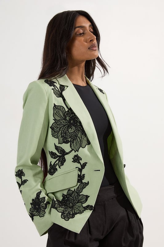 This Karen Millen tailored jacket transforms any ensemble with its exquisite placed floral lace embroidery. The regular fit provides comfortable structure while maintaining a sophisticated silhouette that works beautifully for formal occasions. As seen on our model, pair with sleek black trousers for a contemporary take on evening attire, or style with a coordinating skirt for wedding season elegance. The collared design and single-button closure create a flattering V-shaped opening that elongates the torso. Perfect for summer garden parties, race day events or evening receptions, this jacket offers versatility beyond the ordinary. Layer over a simple camisole or wear with confidence as a statement piece in its own right. The intricate embroidery detail ensures you'll command attention at any formal gathering.  Striking floral lace embroidery creates a dramatic statement across the jacket Tailored silhouette with structured shoulders and a single-button fastening Collared neckline adds a refined touch to this occasion piece Functional front pockets provide both style and practicality Viscose linen blend offers a lightweight feel with natural texture