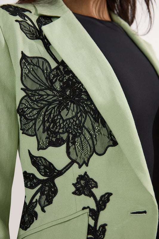 This Karen Millen tailored jacket transforms any ensemble with its exquisite placed floral lace embroidery. The regular fit provides comfortable structure while maintaining a sophisticated silhouette that works beautifully for formal occasions. As seen on our model, pair with sleek black trousers for a contemporary take on evening attire, or style with a coordinating skirt for wedding season elegance. The collared design and single-button closure create a flattering V-shaped opening that elongates the torso. Perfect for summer garden parties, race day events or evening receptions, this jacket offers versatility beyond the ordinary. Layer over a simple camisole or wear with confidence as a statement piece in its own right. The intricate embroidery detail ensures you'll command attention at any formal gathering.  Striking floral lace embroidery creates a dramatic statement across the jacket Tailored silhouette with structured shoulders and a single-button fastening Collared neckline adds a refined touch to this occasion piece Functional front pockets provide both style and practicality Viscose linen blend offers a lightweight feel with natural texture