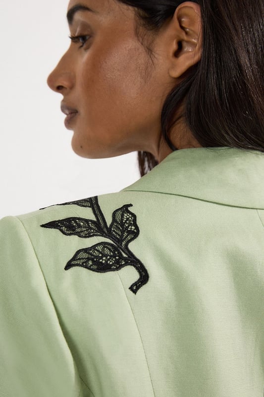 This Karen Millen tailored jacket transforms any ensemble with its exquisite placed floral lace embroidery. The regular fit provides comfortable structure while maintaining a sophisticated silhouette that works beautifully for formal occasions. As seen on our model, pair with sleek black trousers for a contemporary take on evening attire, or style with a coordinating skirt for wedding season elegance. The collared design and single-button closure create a flattering V-shaped opening that elongates the torso. Perfect for summer garden parties, race day events or evening receptions, this jacket offers versatility beyond the ordinary. Layer over a simple camisole or wear with confidence as a statement piece in its own right. The intricate embroidery detail ensures you'll command attention at any formal gathering.  Striking floral lace embroidery creates a dramatic statement across the jacket Tailored silhouette with structured shoulders and a single-button fastening Collared neckline adds a refined touch to this occasion piece Functional front pockets provide both style and practicality Viscose linen blend offers a lightweight feel with natural texture
