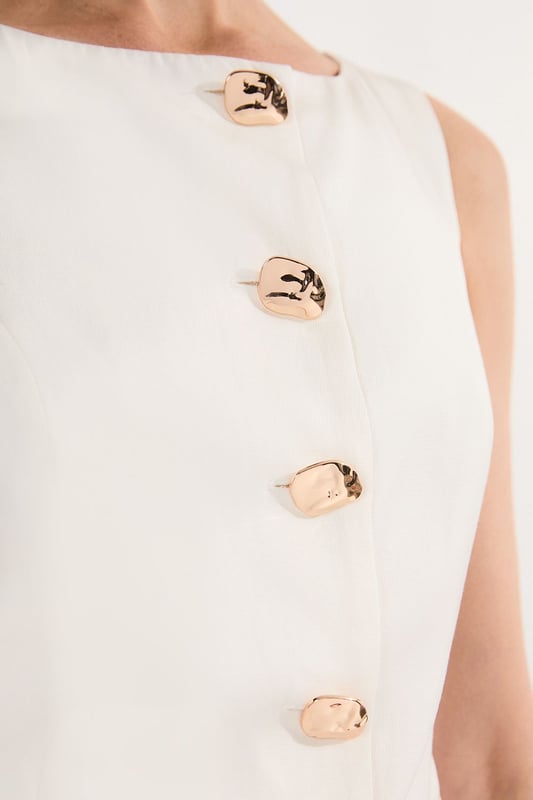 Ease into the new season, surrendering to the return of sunlit afternoons and a relaxed, carefree spirit. Discover contemporary cuts that can be mixed and matched effortlessly - creating a clean and sophisticated aesthetic.  This waistcoat reimagines traditional tailoring with its contemporary silhouette and striking button detail. The linen-viscose blend creates a structured yet breathable piece that maintains its shape beautifully throughout the day. Style with wide-leg trousers as shown for a relaxed daytime ensemble that balances structure with fluidity. For casual gatherings, layer over a crisp white shirt with sleeves rolled up and pair with your favourite straight-leg jeans and leather trainers. This versatile piece transitions effortlessly from office to weekend brunch, simply swap your footwear from flats to ankle boots as the occasion demands. The unique button placement and asymmetrical hem create a distinctive focal point that will refresh your everyday wardrobe staples.  Sleek tailored waistcoat featuring distinctive statement buttons for a contemporary twist Slim fit design with a flattering silhouette that accentuates the waistline Round neckline offering a sophisticated alternative to traditional V-neck waistcoats Asymmetrical hem with a modern front split detail for added visual interest Versatile sleeveless design perfect for layering throughout multiple seasons