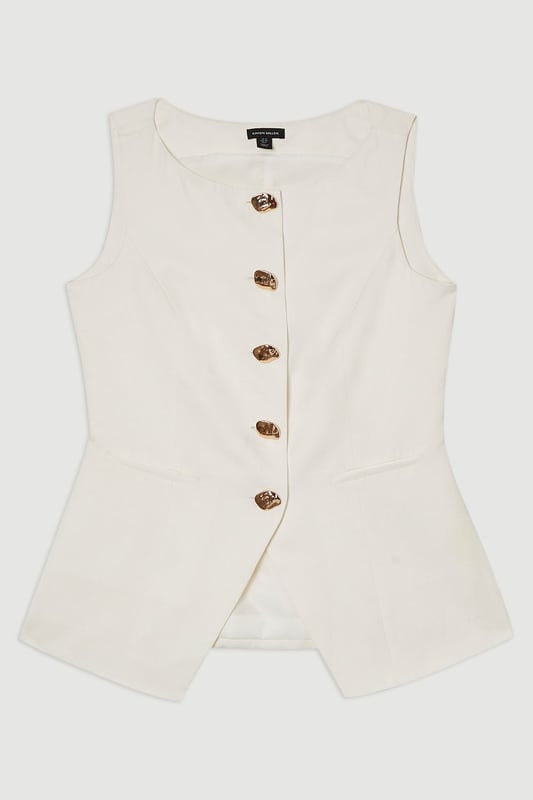 Ease into the new season, surrendering to the return of sunlit afternoons and a relaxed, carefree spirit. Discover contemporary cuts that can be mixed and matched effortlessly - creating a clean and sophisticated aesthetic.  This waistcoat reimagines traditional tailoring with its contemporary silhouette and striking button detail. The linen-viscose blend creates a structured yet breathable piece that maintains its shape beautifully throughout the day. Style with wide-leg trousers as shown for a relaxed daytime ensemble that balances structure with fluidity. For casual gatherings, layer over a crisp white shirt with sleeves rolled up and pair with your favourite straight-leg jeans and leather trainers. This versatile piece transitions effortlessly from office to weekend brunch, simply swap your footwear from flats to ankle boots as the occasion demands. The unique button placement and asymmetrical hem create a distinctive focal point that will refresh your everyday wardrobe staples.  Sleek tailored waistcoat featuring distinctive statement buttons for a contemporary twist Slim fit design with a flattering silhouette that accentuates the waistline Round neckline offering a sophisticated alternative to traditional V-neck waistcoats Asymmetrical hem with a modern front split detail for added visual interest Versatile sleeveless design perfect for layering throughout multiple seasons