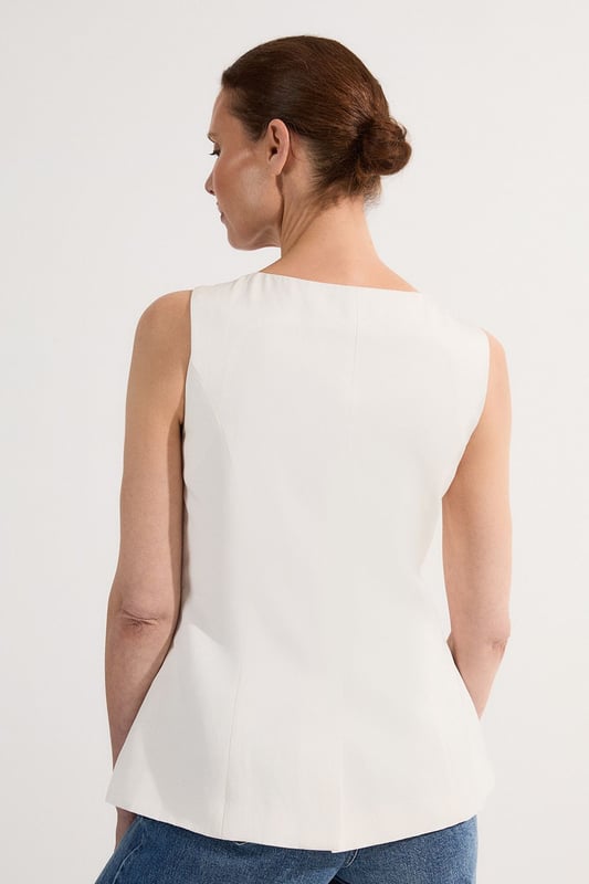 Ease into the new season, surrendering to the return of sunlit afternoons and a relaxed, carefree spirit. Discover contemporary cuts that can be mixed and matched effortlessly - creating a clean and sophisticated aesthetic.  This waistcoat reimagines traditional tailoring with its contemporary silhouette and striking button detail. The linen-viscose blend creates a structured yet breathable piece that maintains its shape beautifully throughout the day. Style with wide-leg trousers as shown for a relaxed daytime ensemble that balances structure with fluidity. For casual gatherings, layer over a crisp white shirt with sleeves rolled up and pair with your favourite straight-leg jeans and leather trainers. This versatile piece transitions effortlessly from office to weekend brunch, simply swap your footwear from flats to ankle boots as the occasion demands. The unique button placement and asymmetrical hem create a distinctive focal point that will refresh your everyday wardrobe staples.  Sleek tailored waistcoat featuring distinctive statement buttons for a contemporary twist Slim fit design with a flattering silhouette that accentuates the waistline Round neckline offering a sophisticated alternative to traditional V-neck waistcoats Asymmetrical hem with a modern front split detail for added visual interest Versatile sleeveless design perfect for layering throughout multiple seasons