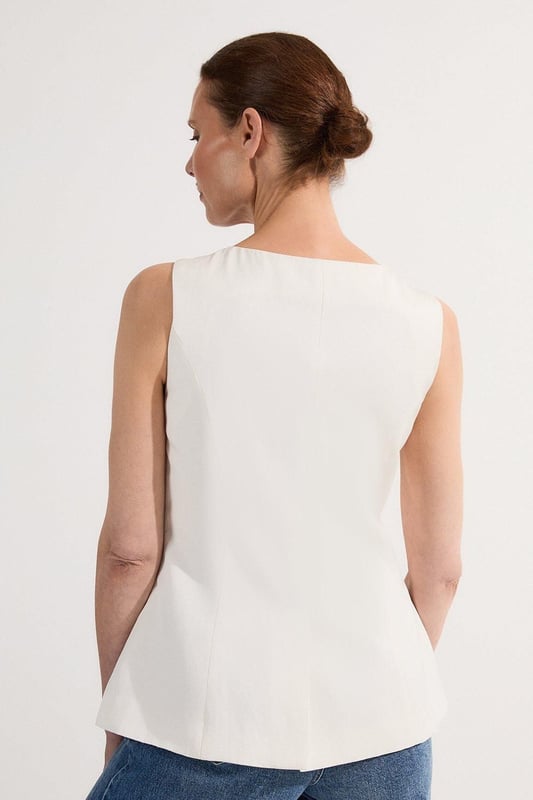 Ease into the new season, surrendering to the return of sunlit afternoons and a relaxed, carefree spirit. Discover contemporary cuts that can be mixed and matched effortlessly - creating a clean and sophisticated aesthetic.  This waistcoat reimagines traditional tailoring with its contemporary silhouette and striking button detail. The linen-viscose blend creates a structured yet breathable piece that maintains its shape beautifully throughout the day. Style with wide-leg trousers as shown for a relaxed daytime ensemble that balances structure with fluidity. For casual gatherings, layer over a crisp white shirt with sleeves rolled up and pair with your favourite straight-leg jeans and leather trainers. This versatile piece transitions effortlessly from office to weekend brunch, simply swap your footwear from flats to ankle boots as the occasion demands. The unique button placement and asymmetrical hem create a distinctive focal point that will refresh your everyday wardrobe staples.  Sleek tailored waistcoat featuring distinctive statement buttons for a contemporary twist Slim fit design with a flattering silhouette that accentuates the waistline Round neckline offering a sophisticated alternative to traditional V-neck waistcoats Asymmetrical hem with a modern front split detail for added visual interest Versatile sleeveless design perfect for layering throughout multiple seasons