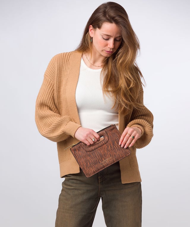 The 'Esher' clutch bag from Pure Luxuries London is handcrafted from luxurious natural leather with a beautifully suede finish. The dual zips, above the built-in handles, secure the dual compartments that come lined with natural, untreated 100% cotton. Additional storage space is provided by a central slip pocket between the zipped compartments, ideal for on-the-go storage. Adorned with the iconic Pure Luxuries London gold foil embossed logo as the perfect finishing touch.