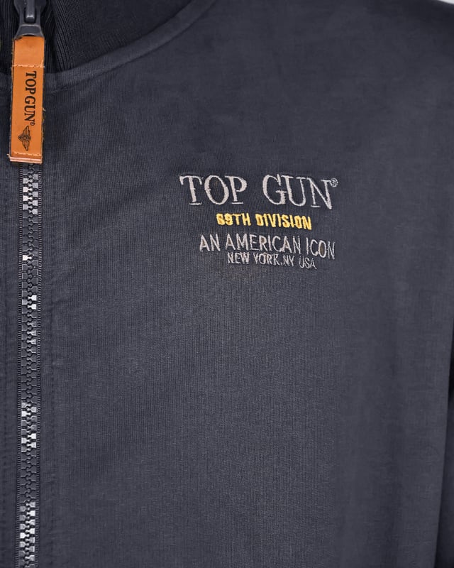 Leichte Top Gun Jacke für die Übergangszeit mit Top Gun Schriftzug auf der Brust. Das Highlight ist der Top Gun Tigerkopf als Print auf der Rückseite der Jacke. Zwei komfortable Seitentaschen mit Zipper sowie zwei Schulterklappen machen diese Jacke zu einem absoluten Muss. Der Strickbund an den Ärmleabschlüssen und dem Saum sorgen für eine ideale Passform.