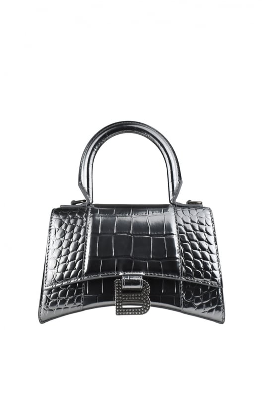 Bolso de mano Balenciaga Hourglass plateado.Piel de becerro grabada en cocodrilo.Placa con logotipo B de la firma en strass.Detalles metálicos plateados.Solapa superior con cierre de botón a presión.Asa redondeada.Bandolera extraíble y ajustable. Medidas: 19 cm x 12 cm x 8 cm.Talla pequeña.Made in Italy.