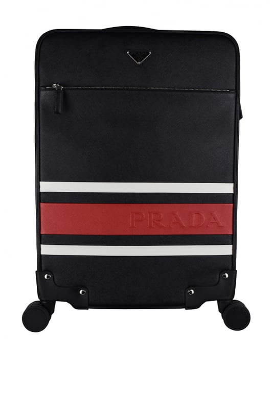 Maleta de cabina Prada en piel saffiano negra.Dos franjas decorativas blancas y una roja con el logotipo de Prada.Logotipo metálico triangular.Bolsillo delantero con cremallera.Un asa de piel y un asa telescópica.Detalles metálicos plateados. Cuatro ruedas.Cierre con cremallera.Dimensiones: 56 x 37 x 23 cm.100% piel.