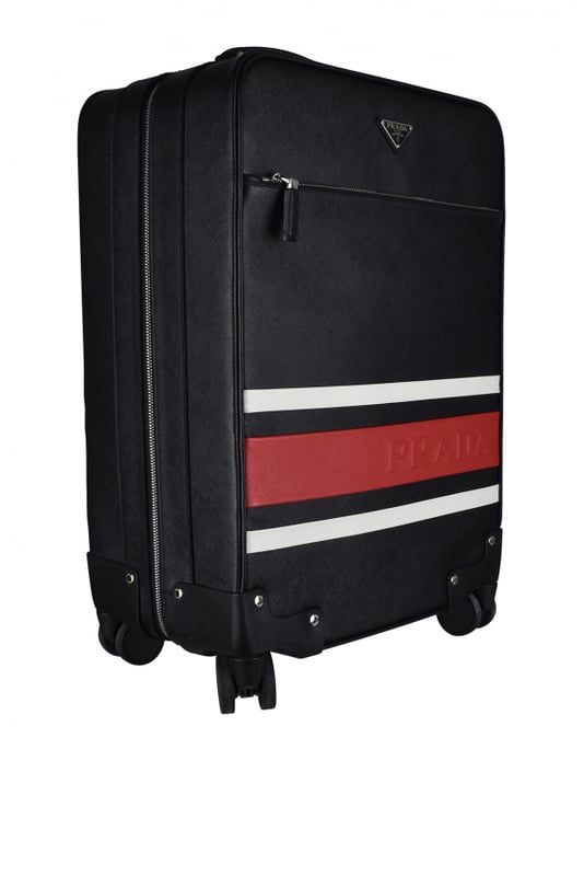 Maleta de cabina Prada en piel saffiano negra.Dos franjas decorativas blancas y una roja con el logotipo de Prada.Logotipo metálico triangular.Bolsillo delantero con cremallera.Un asa de piel y un asa telescópica.Detalles metálicos plateados. Cuatro ruedas.Cierre con cremallera.Dimensiones: 56 x 37 x 23 cm.100% piel.