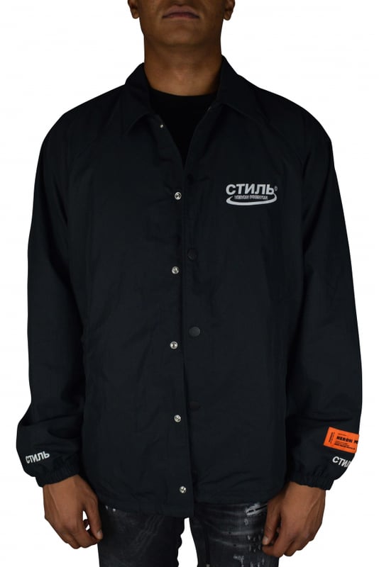 Chaqueta Heron Preston.De color negro.Logotipo impreso en la parte delantera.Cuello con capucha integrada.Parche con logotipo cosido en la manga.Cierre a presión en la parte delantera.Bolsillos laterales.Logotipo en ambos puños cosido en blanco.Parche naranja  HERON PRESTON  en la manga izquierda.Cordón en la cintura.Made in Italy.