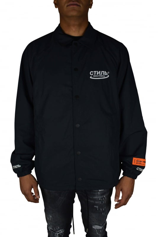 Chaqueta Heron Preston.De color negro.Logotipo impreso en la parte delantera.Cuello con capucha integrada.Parche con logotipo cosido en la manga.Cierre a presión en la parte delantera.Bolsillos laterales.Logotipo en ambos puños cosido en blanco.Parche naranja  HERON PRESTON  en la manga izquierda.Cordón en la cintura.Made in Italy.