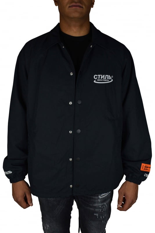 Chaqueta Heron Preston.De color negro.Logotipo impreso en la parte delantera.Cuello con capucha integrada.Parche con logotipo cosido en la manga.Cierre a presión en la parte delantera.Bolsillos laterales.Logotipo en ambos puños cosido en blanco.Parche naranja  HERON PRESTON  en la manga izquierda.Cordón en la cintura.Made in Italy.