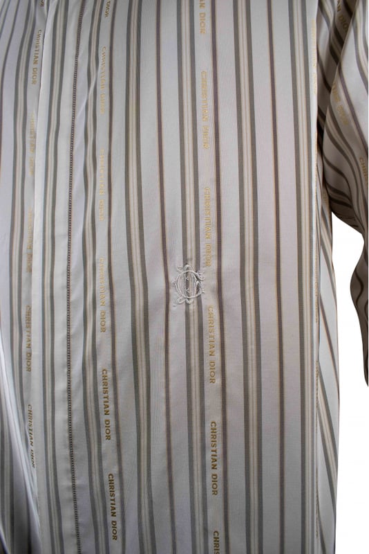 Camisa Christian Dior blanca con rayas grises y doradas.Logotipo Christian Dior bordado en línea con las rayas por toda la camisa.Símbolo  CD  bordado en blanco en la parte delantera de la camisa. Cuello clásico.Mangas largas.61% poliéster 31% seda.Made in Italy.