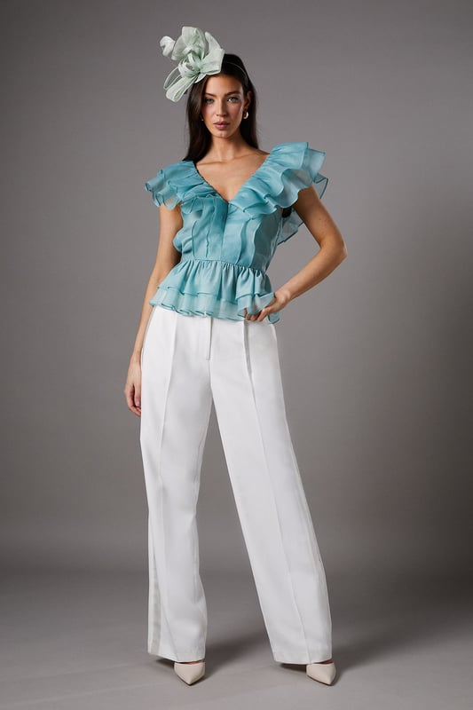 Exquisite organza fabric with delicate texture for a refined finish
        Dramatic V-neckline complemented by cascading frills for a feminine silhouette
        Elegant peplum design creating a flattering waistline definition
        Striking open back with ruffle detailing for added drama
        Tiered hem with multiple layers of frills for dimensional movement
    
    This captivating Coast peplum top showcases the beauty of textured organza with its sumptuous frills and feminine detailing. The striking V-neckline frames the dcolletage beautifully, whilst the peplum silhouette creates a figure-enhancing shape that celebrates the waistline. Perfect for summer race days or wedding celebrations, this top pairs wonderfully with tailored wide-leg trousers as styled on our model. Add a statement fascinator and minimal jewellery to complete your occasion ensemble. For evening events, swap the fascinator for chandelier earrings and a sleek clutch bag. The versatile design works brilliantly for garden parties, formal luncheons or champagne receptions where sophisticated dressing is essential. The open back detail adds an unexpected touch of allure to this otherwise classic piece.