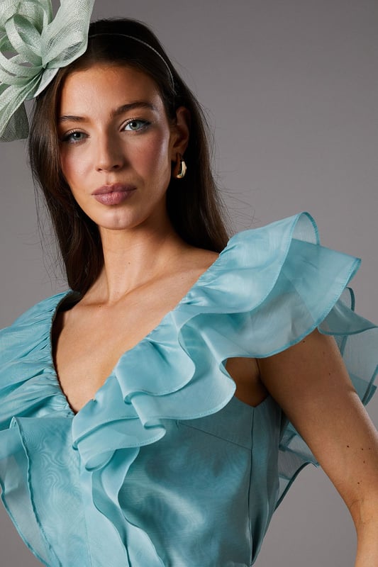 Exquisite organza fabric with delicate texture for a refined finish
        Dramatic V-neckline complemented by cascading frills for a feminine silhouette
        Elegant peplum design creating a flattering waistline definition
        Striking open back with ruffle detailing for added drama
        Tiered hem with multiple layers of frills for dimensional movement
    
    This captivating Coast peplum top showcases the beauty of textured organza with its sumptuous frills and feminine detailing. The striking V-neckline frames the dcolletage beautifully, whilst the peplum silhouette creates a figure-enhancing shape that celebrates the waistline. Perfect for summer race days or wedding celebrations, this top pairs wonderfully with tailored wide-leg trousers as styled on our model. Add a statement fascinator and minimal jewellery to complete your occasion ensemble. For evening events, swap the fascinator for chandelier earrings and a sleek clutch bag. The versatile design works brilliantly for garden parties, formal luncheons or champagne receptions where sophisticated dressing is essential. The open back detail adds an unexpected touch of allure to this otherwise classic piece.