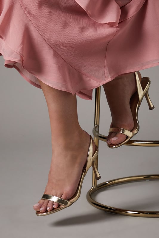Elegant sling back design with delicate barely-there straps for a sophisticated silhouette
        Medium heel height of 5-6.5cm offers the perfect balance of comfort and style
        Sleek metallic finish that catches the light beautifully with every step
        Secure adjustable sling back strap ensures a comfortable, customised fit
        Versatile design that complements both daytime and evening occasion wear
    
    The Vallen Sling Back Sandals from Coast present the quintessential occasion footwear for the discerning woman. These medium-heeled sandals feature a minimalist barely-there design that showcases the foot beautifully whilst providing elegant support. The metallic finish adds a touch of glamour that pairs wonderfully with flowing dresses, as shown with the layered chiffon dress in the imagery. Perfect for weddings, race days and formal gatherings where sophistication is paramount, these sandals will carry you through the day with grace. Style with a structured clutch bag and delicate jewellery for a coordinated ensemble. The modest heel height ensures you can dance the night away or stand comfortably throughout day-long events without compromising on style. These versatile sandals will become a treasured addition to your occasion wardrobe for seasons to come.