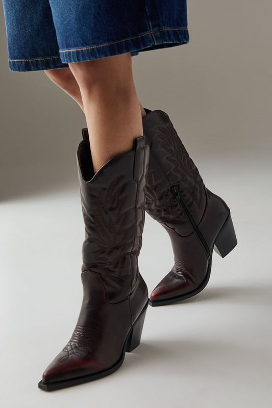 Striking western-inspired calf boots with intricate embroidered detailing
        Brushed faux leather finish for a sophisticated texture
        Pointed toe design with classic pull tabs for easy wear
        Statement 7-9cm block heel adds height whilst maintaining stability
        Calf-height shaft with distinctive western stitching pattern
    
    The Faith Nash Western Boots bring countryside charm to city streets with their distinctive embroidered detailing and brushed finish. The 7-9cm heel creates a flattering silhouette whilst remaining comfortable for all-day wear. Style these versatile boots with a floaty midi dress and oversized jacket for weekend brunches, or pair with straight-leg jeans and a crisp white tee for casual gatherings. For autumn outings, match with a mini skirt and fringed jacket to showcase the boots' western heritage. The pointed toe and sleek silhouette ensure these boots transition effortlessly from day to night, making them a wardrobe essential that combines practicality with statement style. Their classic design promises longevity beyond seasonal trends.