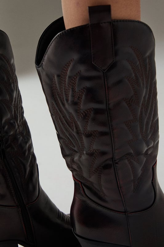 Striking western-inspired calf boots with intricate embroidered detailing
        Brushed faux leather finish for a sophisticated texture
        Pointed toe design with classic pull tabs for easy wear
        Statement 7-9cm block heel adds height whilst maintaining stability
        Calf-height shaft with distinctive western stitching pattern
    
    The Faith Nash Western Boots bring countryside charm to city streets with their distinctive embroidered detailing and brushed finish. The 7-9cm heel creates a flattering silhouette whilst remaining comfortable for all-day wear. Style these versatile boots with a floaty midi dress and oversized jacket for weekend brunches, or pair with straight-leg jeans and a crisp white tee for casual gatherings. For autumn outings, match with a mini skirt and fringed jacket to showcase the boots' western heritage. The pointed toe and sleek silhouette ensure these boots transition effortlessly from day to night, making them a wardrobe essential that combines practicality with statement style. Their classic design promises longevity beyond seasonal trends.