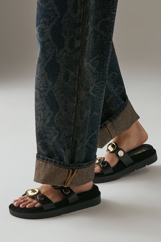Faux leather double strap design with distinctive metal disk detailing
        Comfortable footbed construction for all-day wear
        Low heel height between 2.5-4.5cm offers subtle elevation
        Secure adjustable straps for a customised fit
        Durable synthetic outsole provides reliable grip and traction
    
    The Rhonda mules from Faith combine contemporary style with everyday comfort. These versatile sandals feature eye-catching metal disk detailing that adds a touch of sophistication to casual outfits. As shown in the images, they pair beautifully with wide-leg trousers for an effortlessly chic look. The low heel provides just the right amount of height whilst maintaining walkability, making these mules perfect for family gatherings, weekend brunches or casual shopping trips. The footbed construction moulds to your feet for lasting comfort throughout the day, whilst the double strap design ensures they stay securely in place. Style them with cropped jeans and a crisp white shirt for daytime outings, or match with a flowing maxi dress for relaxed summer evenings.