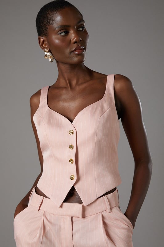 Elegant pinstripe crepe waistcoat with flattering V-neckline
        Strappy design with wide shoulder straps for comfortable wear
        Decorative gold-tone button fastening down the front
        Tailored fit with a slightly cropped silhouette
        Versatile separate that can be styled as part of a coordinating set
    
    This sophisticated Coast waistcoat offers a contemporary twist on traditional tailoring. The strappy design and V-neckline create a feminine silhouette whilst maintaining a structured, polished appearance. Style as seen with the matching wide-leg trousers for a refined coordinating ensemble perfect for summer occasions. For race day elegance, pair with a fascinator and statement earrings, or dress down for garden parties with delicate sandals and a clutch bag. The versatile piece transitions beautifully from day to evening events-simply add a tailored blazer for cooler evenings. The structured crepe fabric holds its shape beautifully whilst offering comfort throughout your special occasion. A timeless investment piece that will become a cornerstone of your occasion wardrobe for seasons to come.