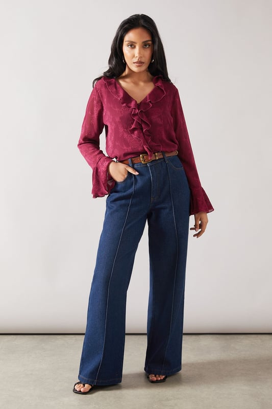 Elegant jacquard fabric with subtle textured pattern throughout
        Feminine ruffle detail cascading down the front
        V-neckline framed by delicate ruffles for a sophisticated touch
        Flared bell sleeves with ruffle trim for added movement
        Relaxed silhouette perfect for petite frames
    
    This charming Wallis blouse combines sophistication with everyday wearability. The jacquard fabric presents a subtle textured pattern that catches the light beautifully, whilst the cascading ruffle detail adds a feminine flourish to your daytime ensemble. Style with your favourite denim jeans and white trainers for casual family gatherings, or tuck into tailored trousers with ballet flats for lunch with friends. The bell sleeves create elegant movement as you go about your day, making this piece both practical and pretty. Layer under a cardigan when the temperature drops or wear alone with statement earrings to showcase the beautiful neckline detail. This versatile blouse transitions effortlessly from shopping trips to informal dinners, making it a wardrobe essential for the sophisticated woman who values both comfort and style.