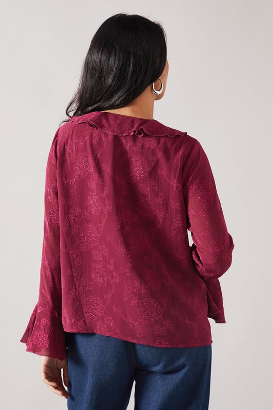 Elegant jacquard fabric with subtle textured pattern throughout
        Feminine ruffle detail cascading down the front
        V-neckline framed by delicate ruffles for a sophisticated touch
        Flared bell sleeves with ruffle trim for added movement
        Relaxed silhouette perfect for petite frames
    
    This charming Wallis blouse combines sophistication with everyday wearability. The jacquard fabric presents a subtle textured pattern that catches the light beautifully, whilst the cascading ruffle detail adds a feminine flourish to your daytime ensemble. Style with your favourite denim jeans and white trainers for casual family gatherings, or tuck into tailored trousers with ballet flats for lunch with friends. The bell sleeves create elegant movement as you go about your day, making this piece both practical and pretty. Layer under a cardigan when the temperature drops or wear alone with statement earrings to showcase the beautiful neckline detail. This versatile blouse transitions effortlessly from shopping trips to informal dinners, making it a wardrobe essential for the sophisticated woman who values both comfort and style.