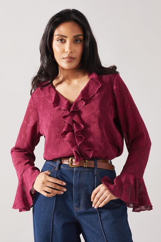 Elegant jacquard fabric with subtle textured pattern throughout
        Feminine ruffle detail cascading down the front
        V-neckline framed by delicate ruffles for a sophisticated touch
        Flared bell sleeves with ruffle trim for added movement
        Relaxed silhouette perfect for petite frames
    
    This charming Wallis blouse combines sophistication with everyday wearability. The jacquard fabric presents a subtle textured pattern that catches the light beautifully, whilst the cascading ruffle detail adds a feminine flourish to your daytime ensemble. Style with your favourite denim jeans and white trainers for casual family gatherings, or tuck into tailored trousers with ballet flats for lunch with friends. The bell sleeves create elegant movement as you go about your day, making this piece both practical and pretty. Layer under a cardigan when the temperature drops or wear alone with statement earrings to showcase the beautiful neckline detail. This versatile blouse transitions effortlessly from shopping trips to informal dinners, making it a wardrobe essential for the sophisticated woman who values both comfort and style.