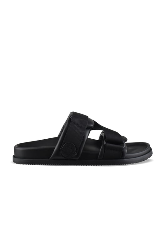 Mon Summer-slipper van zwart Moncler-leer.Gekruiste bandjes van polyester met logo.Klittenbandsluitingen.Logopatch aan de buitenkant.Platte zool.Made in Italy.