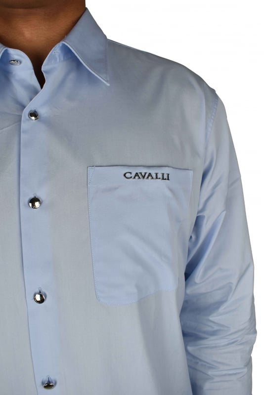 Camisa azul claro Roberto Cavalli.Bolsillo de parche con logotipo de monedas metálicas plateadas en el pecho.Parche con logotipo en la nuca.Cuello en punta.Mangas largas con puños de botones plateados.Cierre con botones plateados en la parte delantera.Made in Italy.