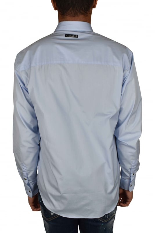 Camisa azul claro Roberto Cavalli.Bolsillo de parche con logotipo de monedas metálicas plateadas en el pecho.Parche con logotipo en la nuca.Cuello en punta.Mangas largas con puños de botones plateados.Cierre con botones plateados en la parte delantera.Made in Italy.