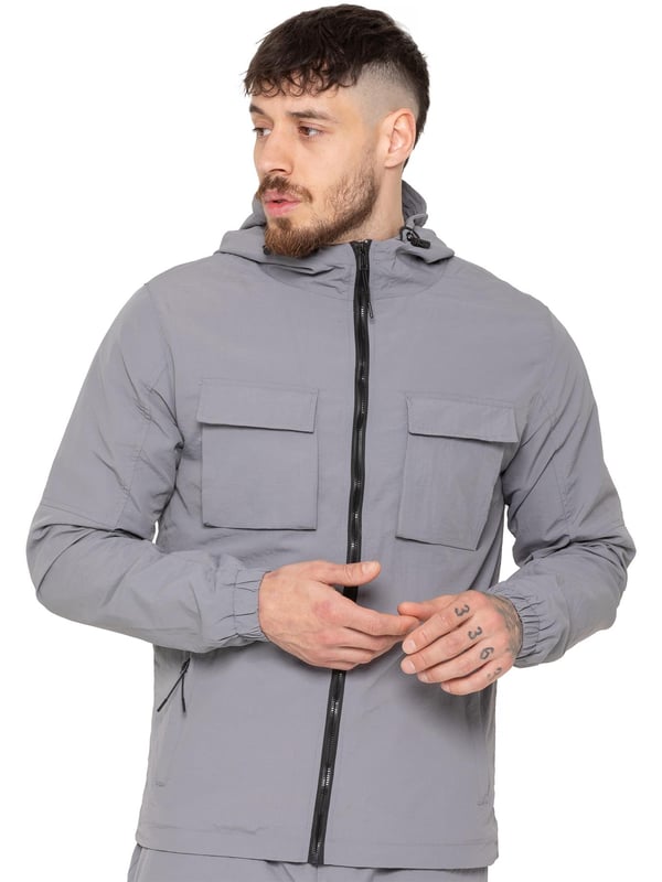 The Enzo Milano Men’s Lightweight Cargo Jacket is a sleek, functional outer layer made from water-repellent crushed poly fabric with a breathable mesh lining for all-day comfort. Designed in a regular fit, it features a full zip front, high neck, and adjustable drawcord hood for versatile coverage. With two Velcro chest pockets, two zippered side pockets, elasticated cuffs, and an adjustable drawcord hem, it offers both style and practicality—perfect for layering in changing weather.