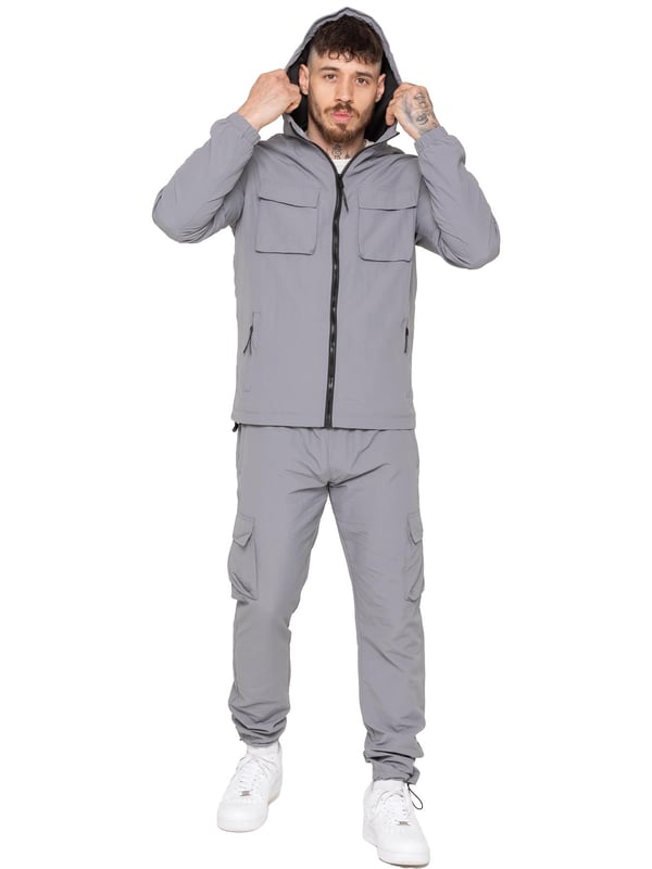 The Enzo Milano Men’s Lightweight Cargo Jacket is a sleek, functional outer layer made from water-repellent crushed poly fabric with a breathable mesh lining for all-day comfort. Designed in a regular fit, it features a full zip front, high neck, and adjustable drawcord hood for versatile coverage. With two Velcro chest pockets, two zippered side pockets, elasticated cuffs, and an adjustable drawcord hem, it offers both style and practicality—perfect for layering in changing weather.